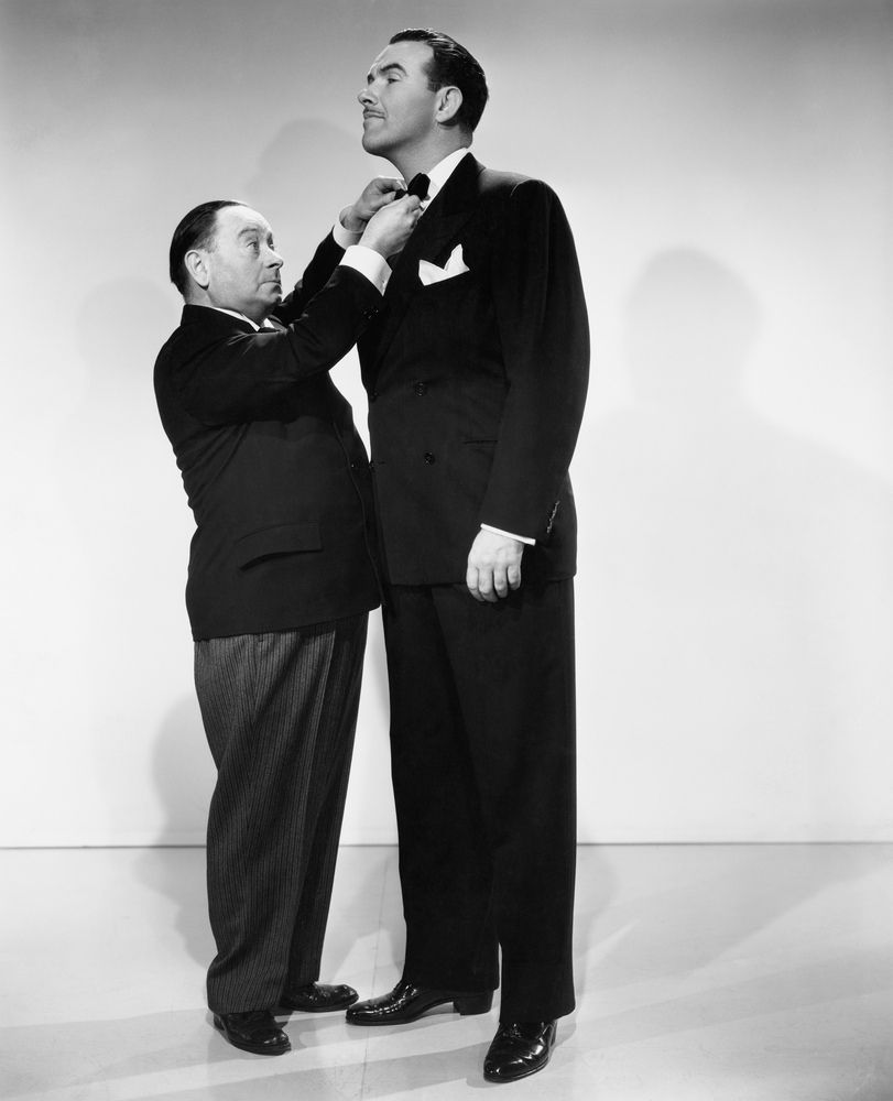 A short man fixes bow tie of taller man.