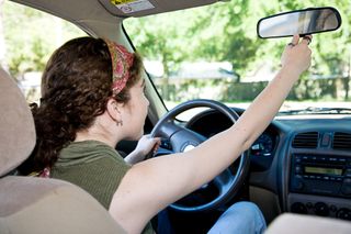 A teen girl adjusts her rearview mirror before driving.