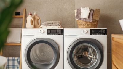 A tumble dryer and washing maching with laundry products and basket on top 