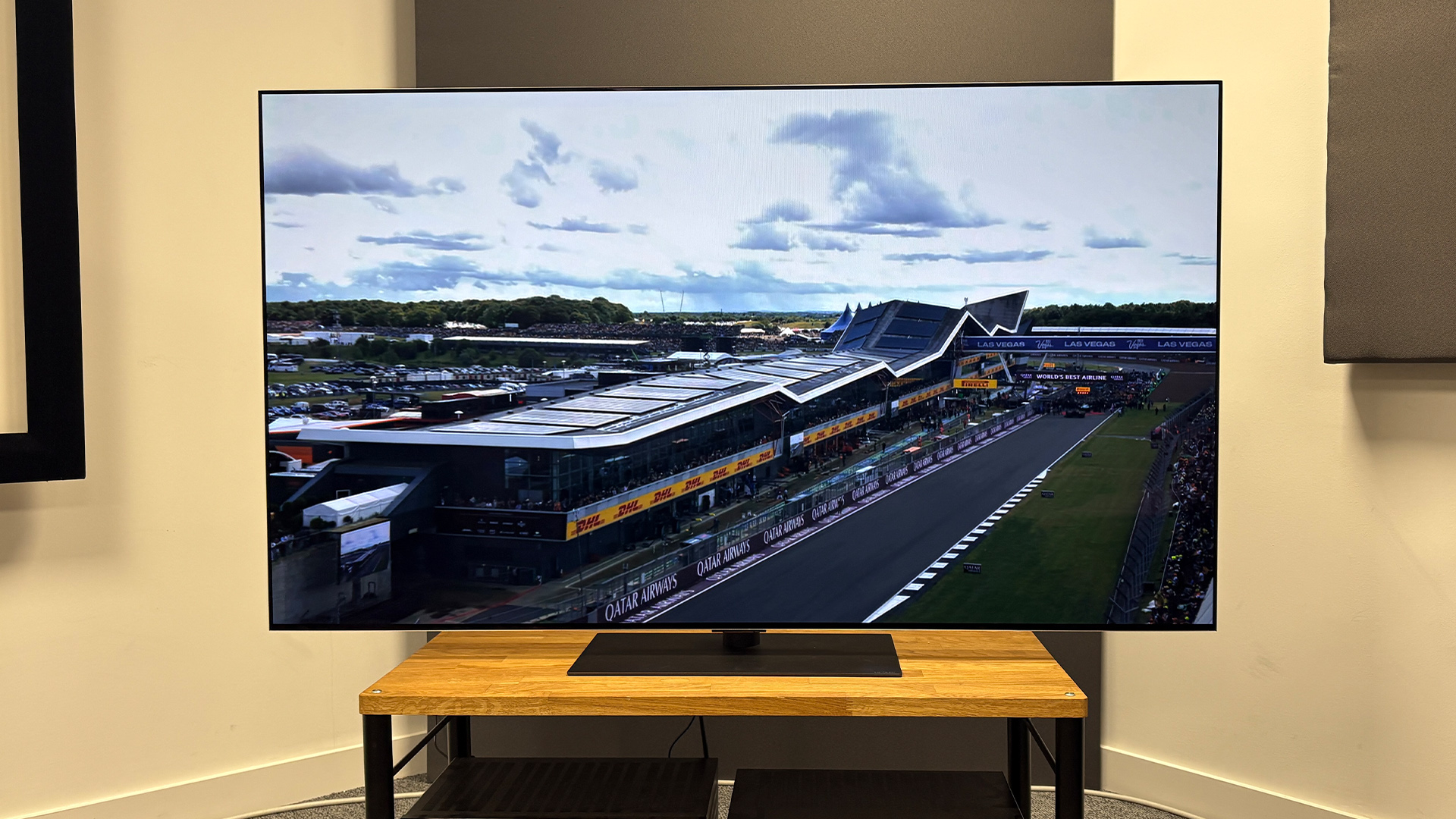 The 65-inch LG G5 OLED TV pictured on a wooden rack. On the screen is a still from Netflix F1 series Drive to Survive.