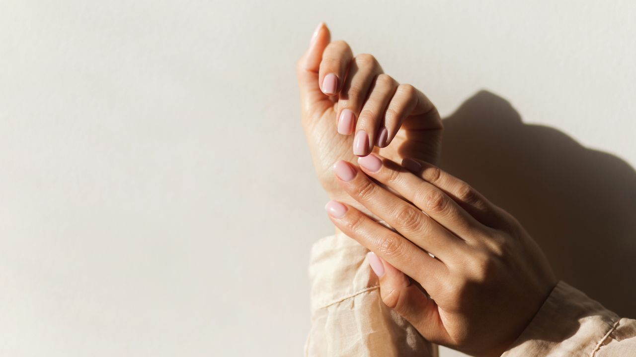 Image showing manicured hands with pink nail polish against an ivory background