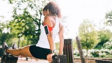 Runner performs a tricep dip outdoors between a bench and a bin