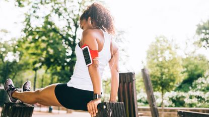 Runner performs a tricep dip outdoors between a bench and a bin