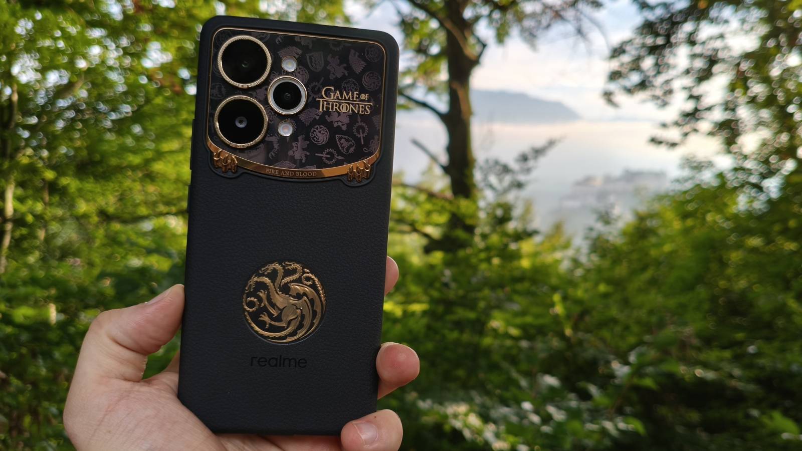 The Realme 15 Pro Game of Thrones Edition ahead of a leafy background and a distant fortress.