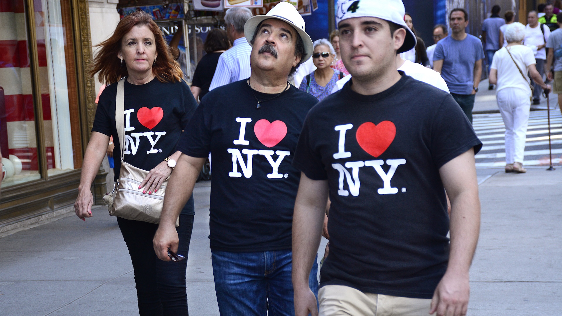 Three New York City visitors wearing matching 'I Love New York' T-shirts walk down Fifth Avenue in Midtown Manhattan.
