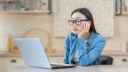 A young woman looks at her laptop, looking a bit concerned or confused.