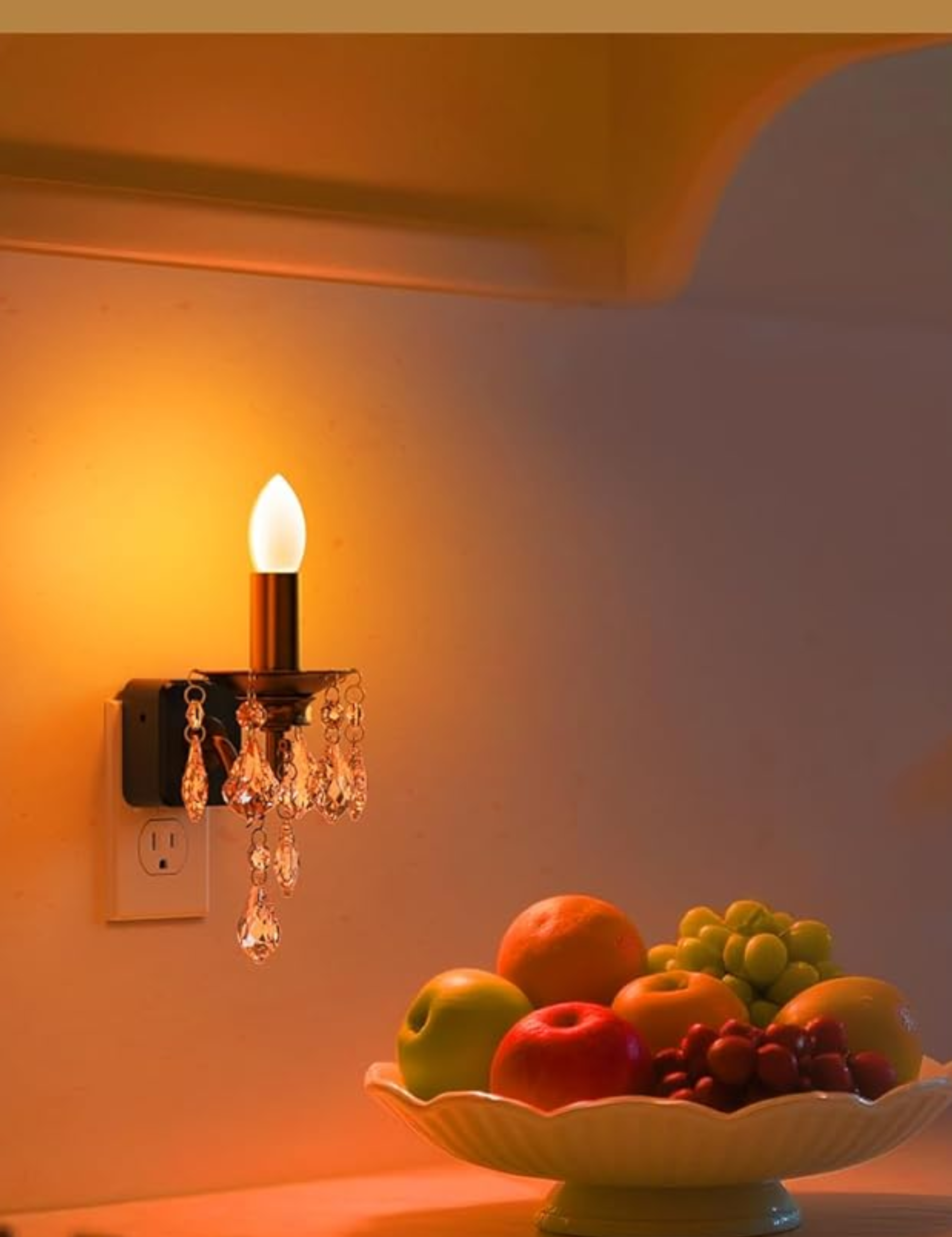 Amazon candle night light decorated with cascade of crystals set inside of an electrical outlet above a kitchen countertop, which is styled with a pedestal bowl of mixed fruit