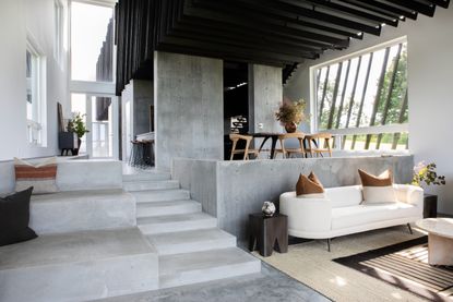 A modern open plan living area with a raised cement dining area, soft furnishings, and cement architectural features