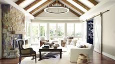 Large vaulted ceiling wooden beamed living room with stone fireplace and neutral furniture