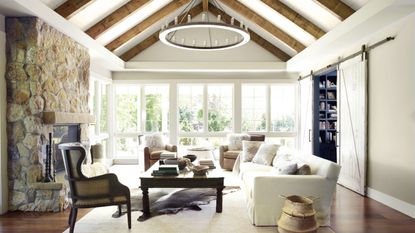 Large vaulted ceiling wooden beamed living room with stone fireplace and neutral furniture