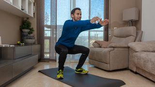 Man performs unweighted squat leg exercise at home