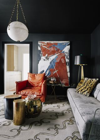 A black living room with a bright artwork and a pop orange chair