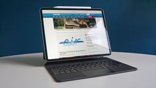 Bästa iPad: En iPad Pro 12.9 (2022) står öppnad på ett vitt skrivbord framför en blå vägg, med TechRadar-hemsidan öppnad på skärmen.