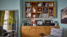 A living room with blue color-drenched walls, a large wooden cabinet with vintage decor, and a matching wooden wall unit above, with styled decor and books. 
