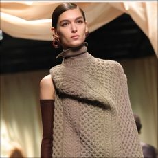 A model walks the runway at milan fashion week wearing a folded cable knit sweater to illustrate a story about wearing versus styling
