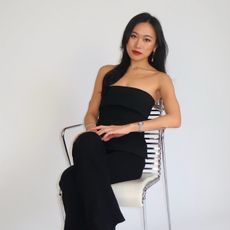 Freja NYC founder, Jenny Lei, sits on metallic chair against white backdrop looking at the camera.
