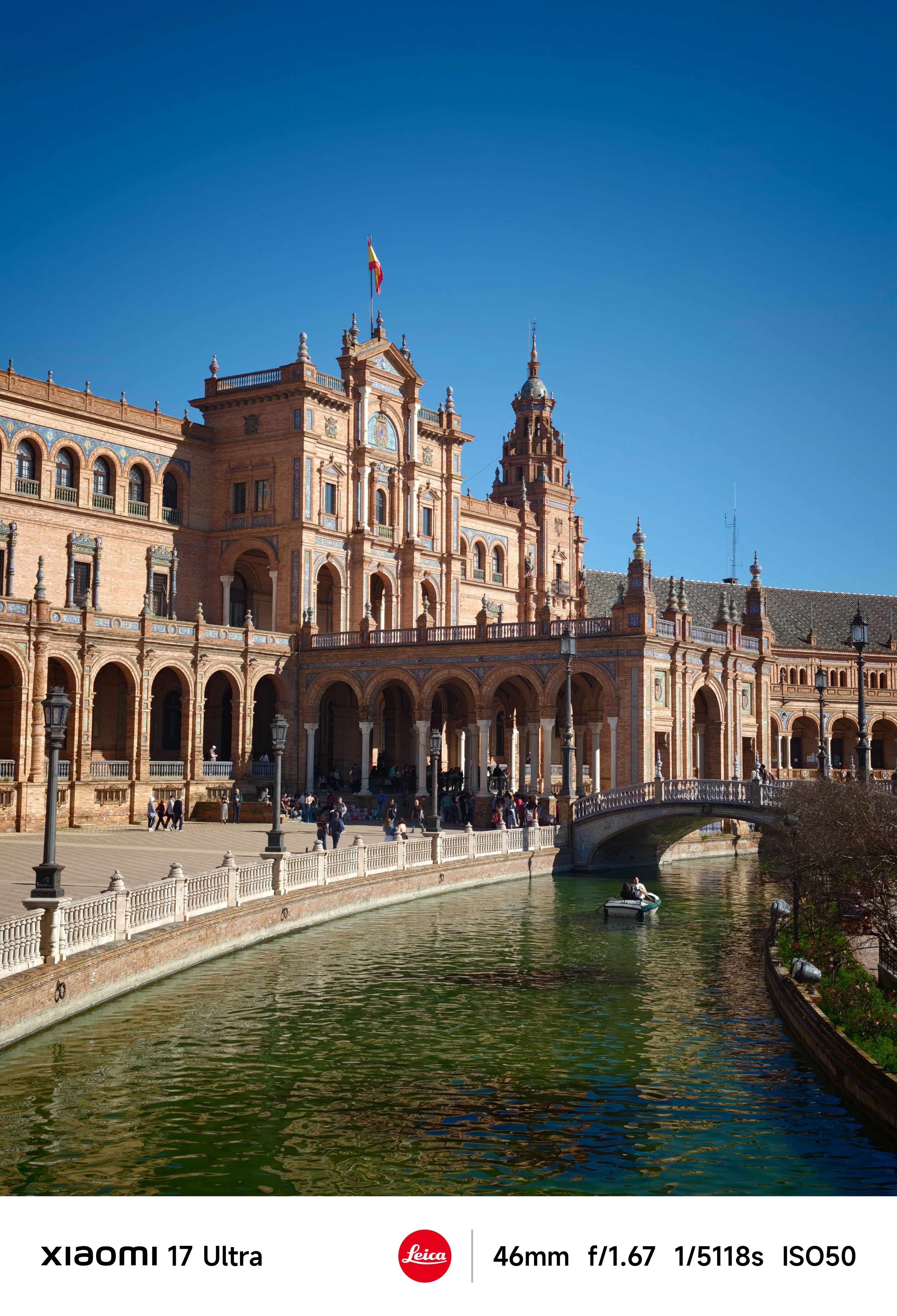 Plaza de Espa&ntilde;a with arched colonnades and canal, a small boat drifting beneath a bridge.