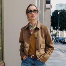 Woman wears brown suede jacket, brown knit, blue jeans and floral scarf