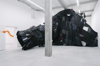 Large art piece made from dark fabric against white walls on the ground floor - by artist Marcin Dudek