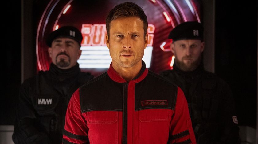 Glen Powell as Ben Richards in The Running Man stood in front of two guards