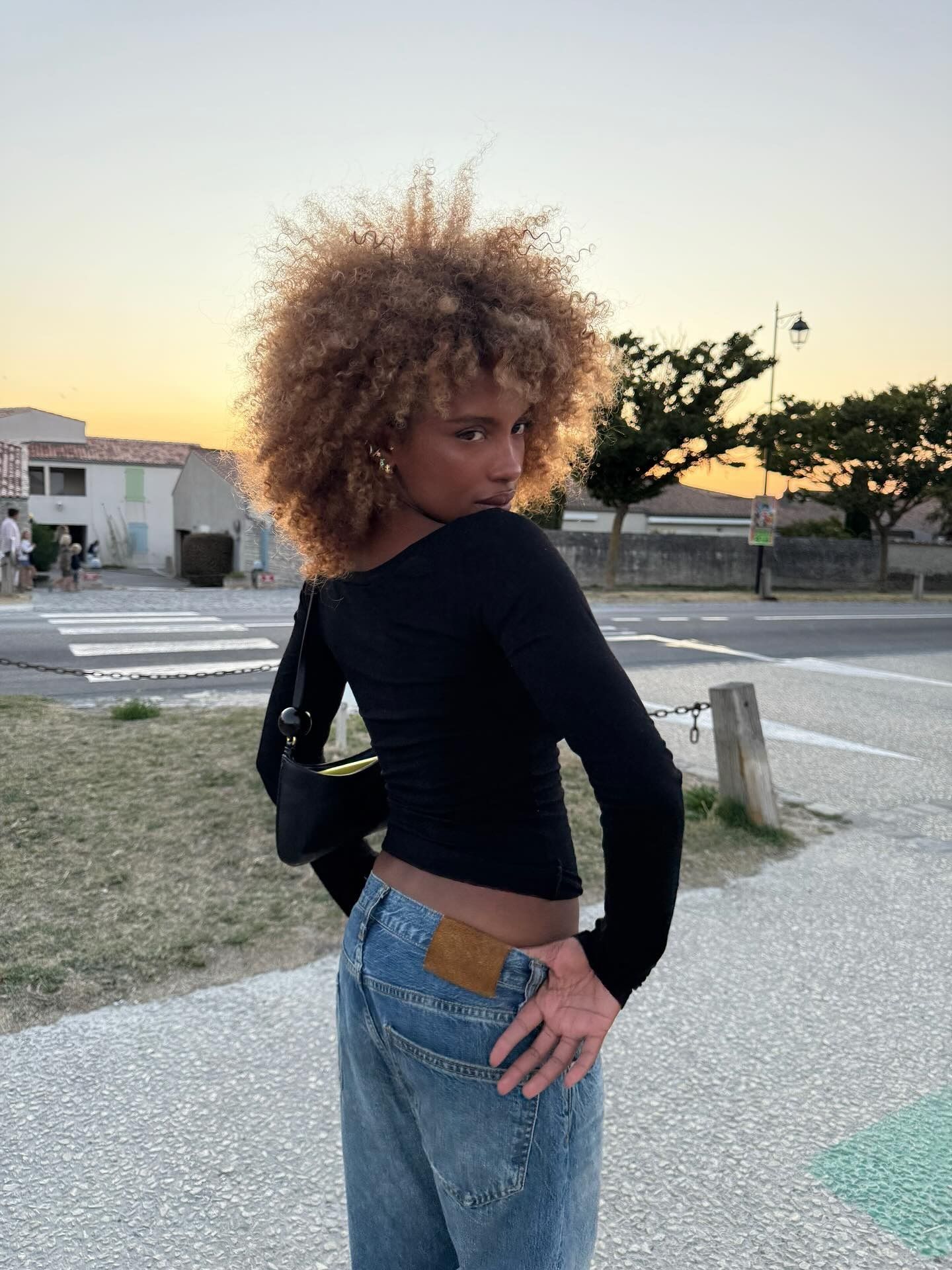 A woman on holiday wearing a black off-the-shoulder top with curly, caramel bronde hair