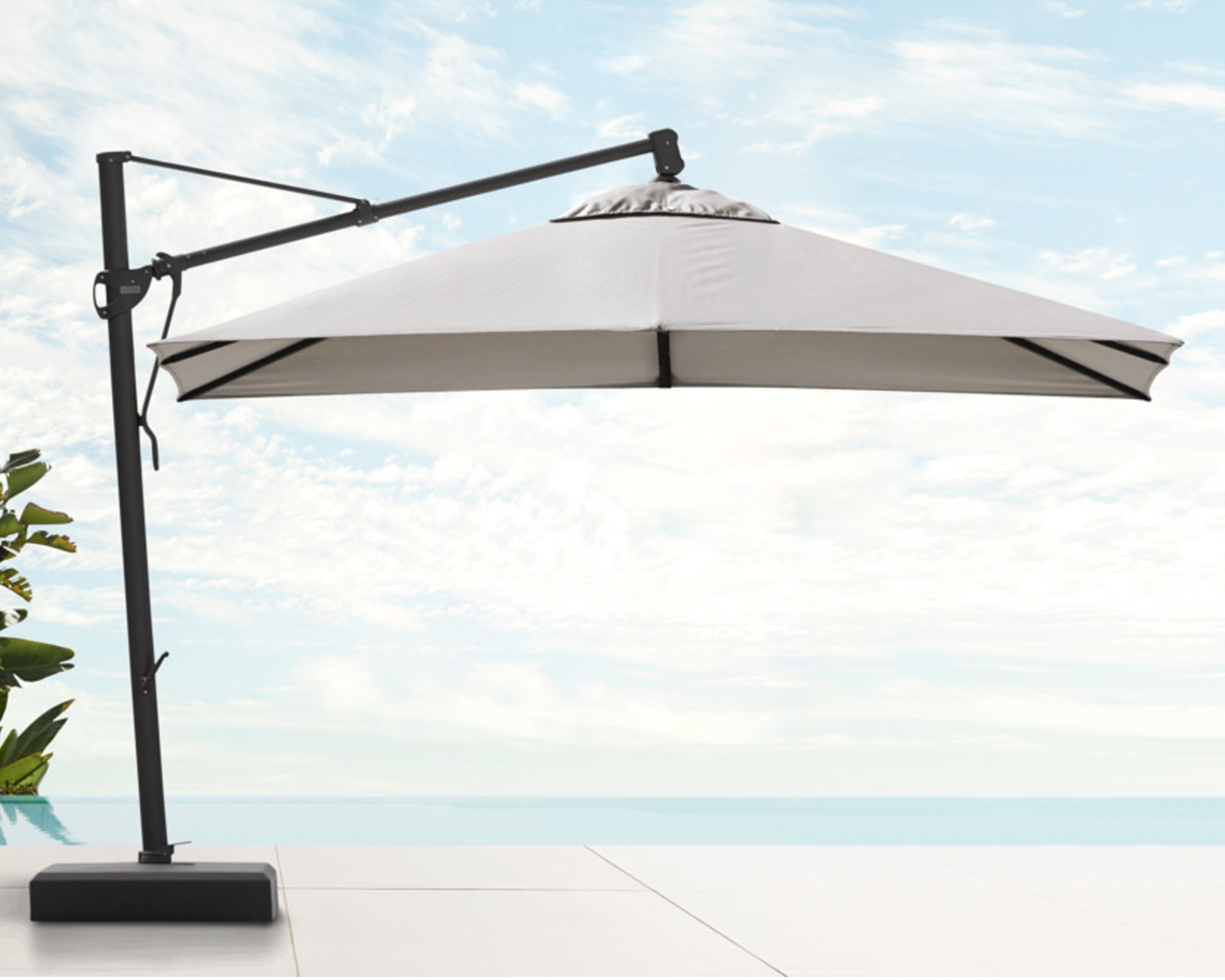 An off-white cantilever umbrella with a black base by the side of a swimming pool