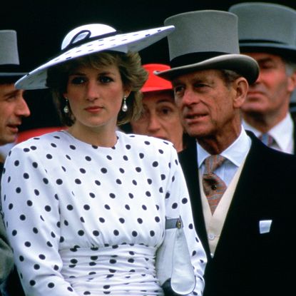 Princess Diana wearing a white polka dot dress and hat looking sullen next to Prince Philip at the Epsom Derby