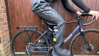 Female cyclist wearing the B Twin 100 City Cycling Rain Overtrousers.