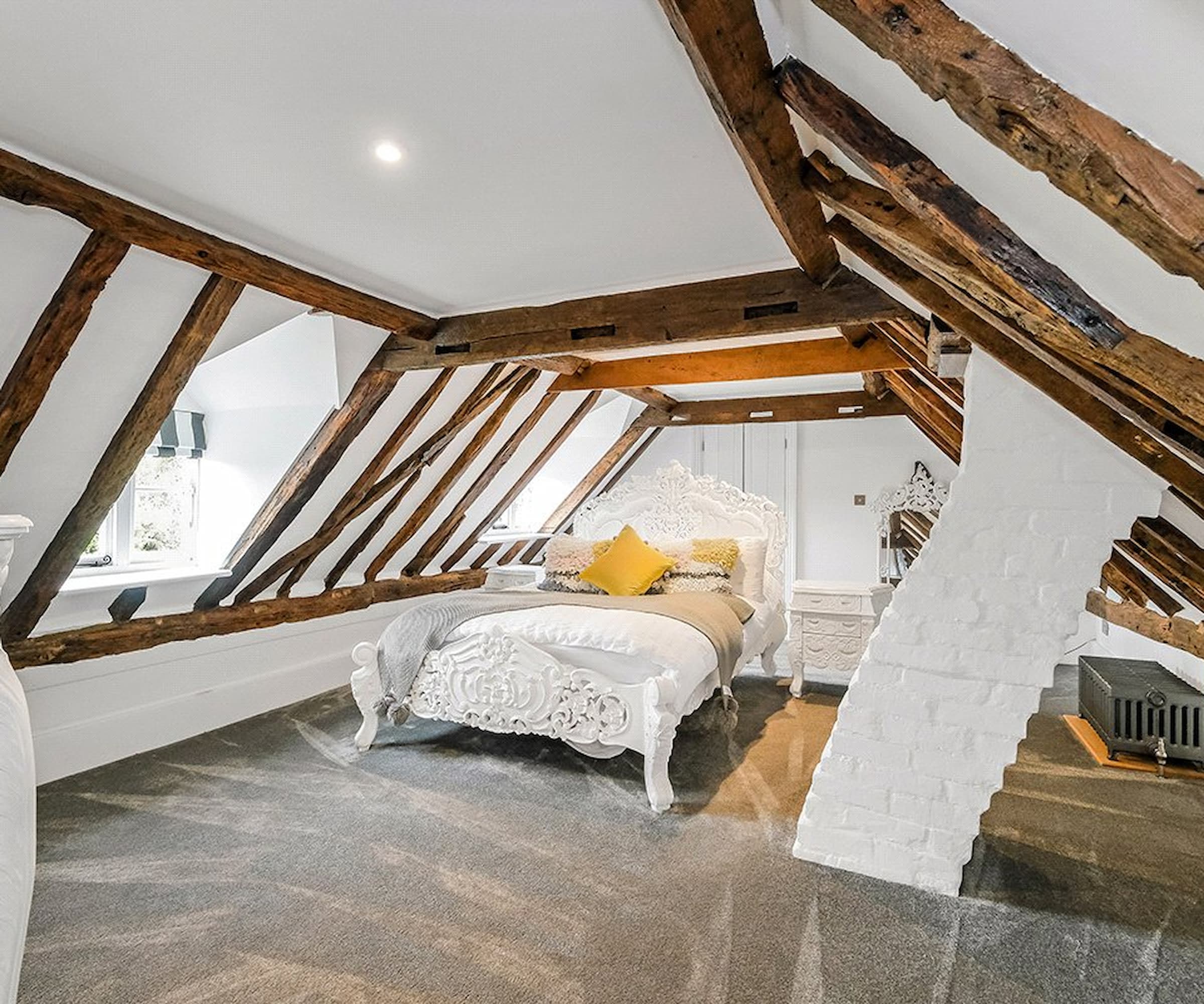 A loft bedroom with vaulted ceiling and oak beams lining the roof and a dormer window