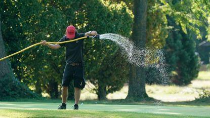 A greenkeeper watering a golf-course green
