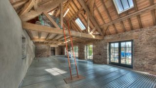 The first floor of a barn in the process of being converted, with timber clad-ceiling, timber beams and stone walls. The floor features an innovative high-strength suspended flooring system from CDI Innovative Construction Materials.