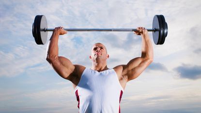 A man lifts a heavy barbell over his head.
