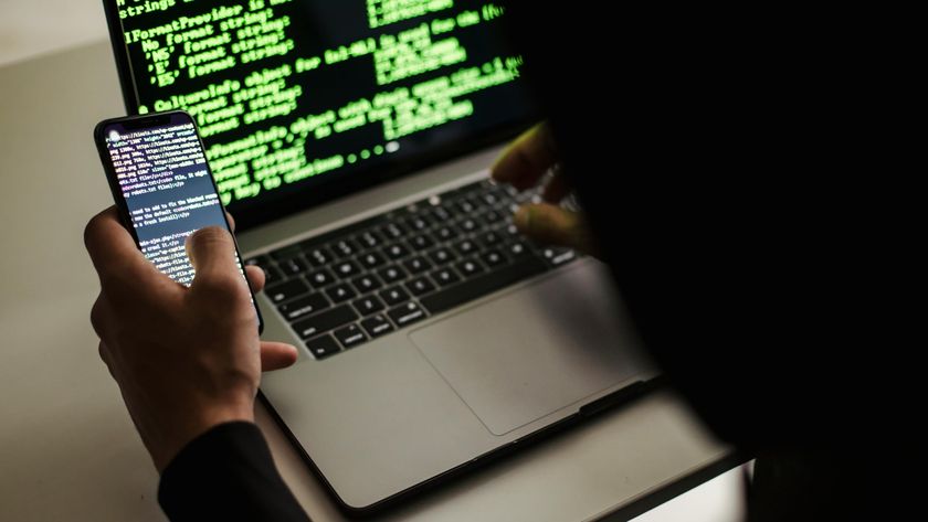 A hacker typing on a MacBook laptop with code on the screen.