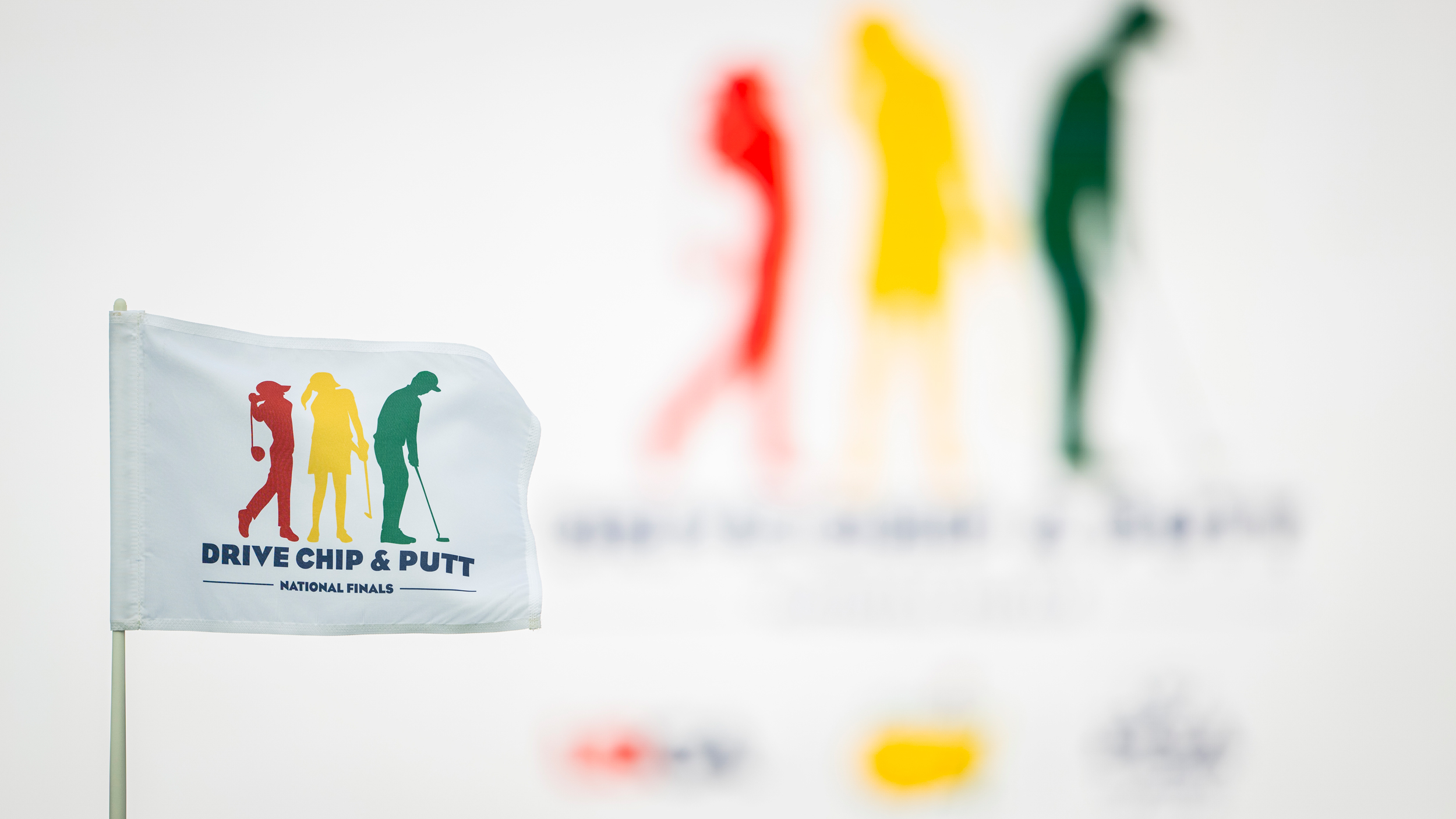 The Drive, Chip and Putt logo on a white flag with the same logo blurred in the background