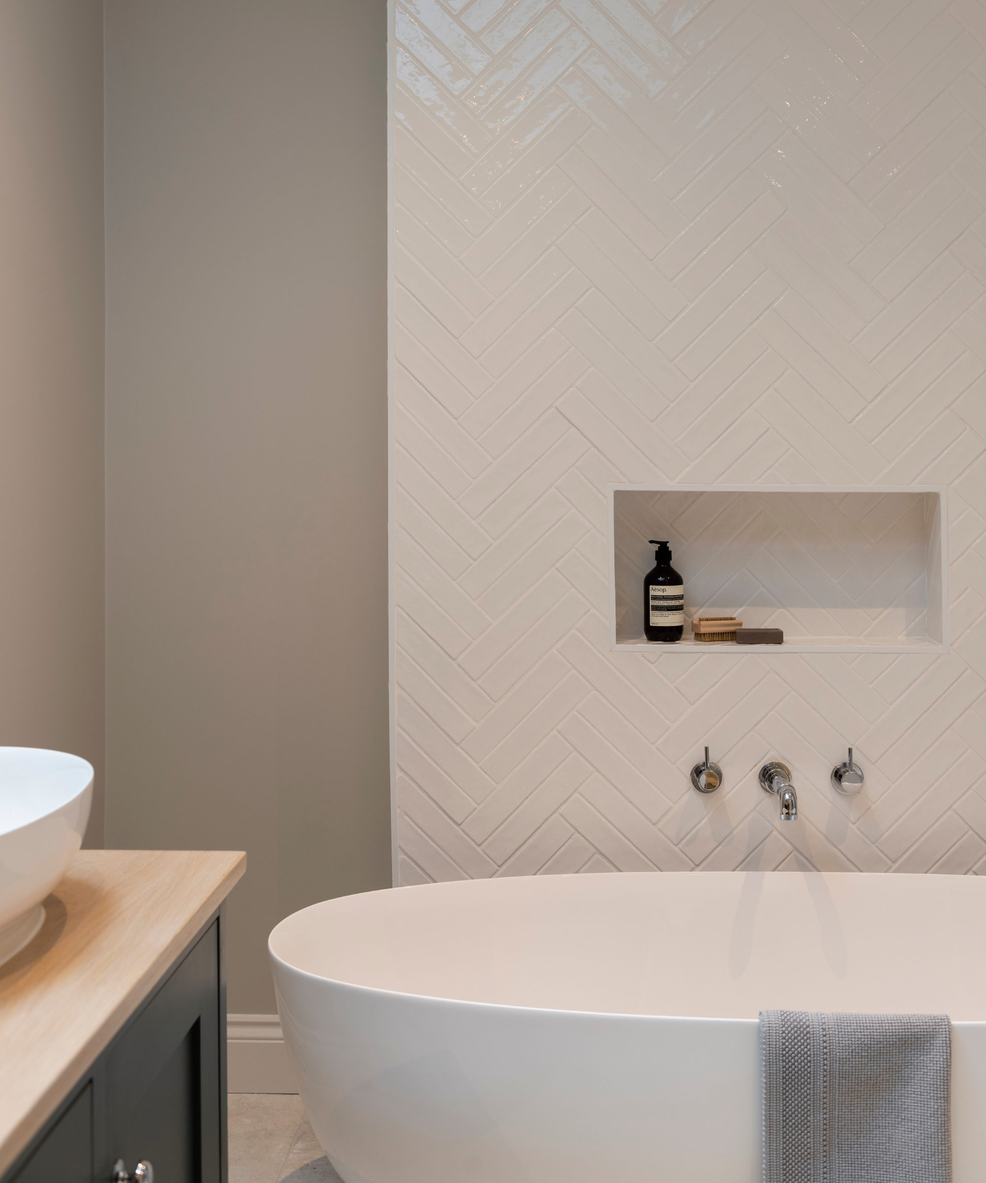 bathroom with large white freestanding bath, tiled wall and shelf inset into wall