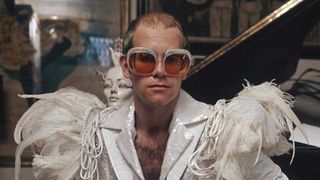 Elton John in a flamboyant stage outfit of white suit with feather trim and rhinestone encrusted glasses, circa 1973. 