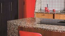 angled terrazzo kitchen island with red chairs, black cabinets, square tiles with pink grout, and timber joinery 