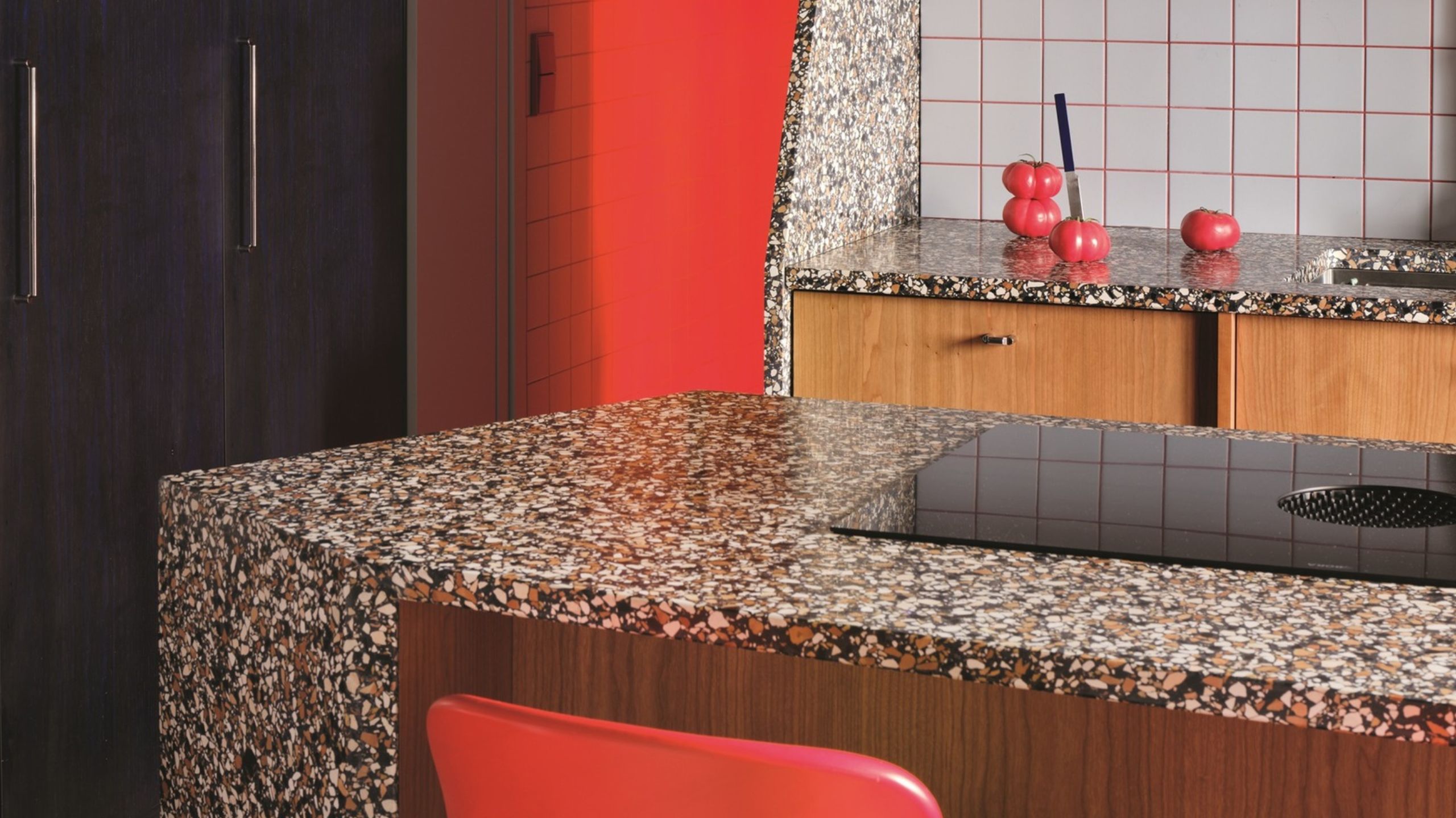 angled terrazzo kitchen island with red chairs, black cabinets, square tiles with pink grout, and timber joinery 