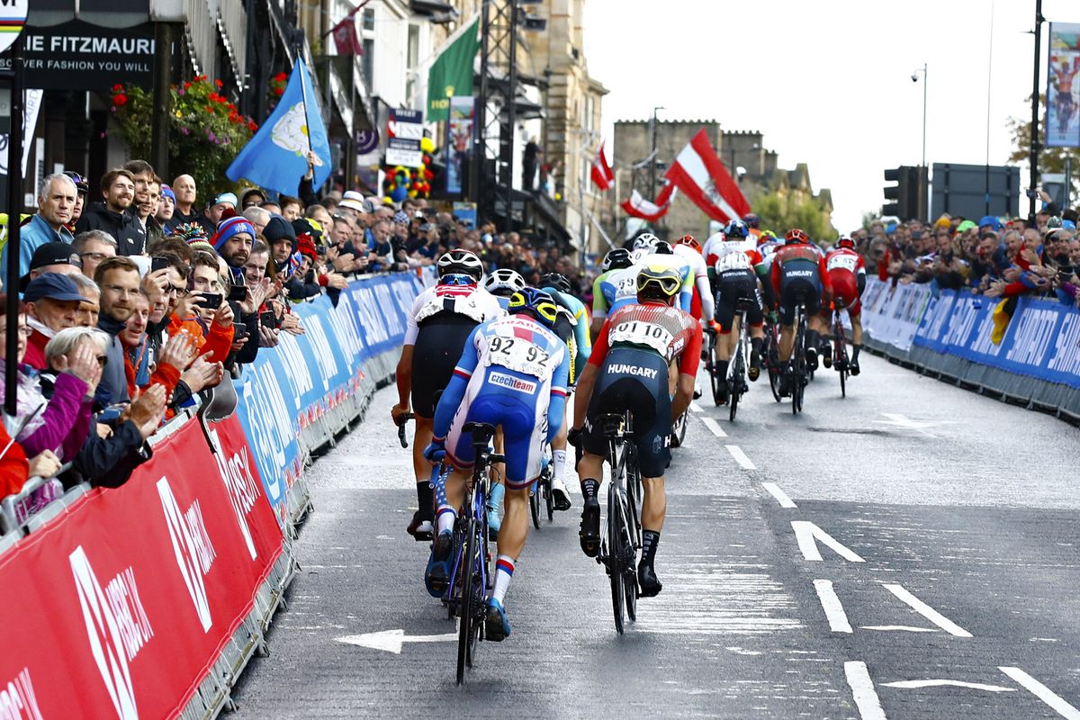 The U23 peloton is strung out passing through the start/finish