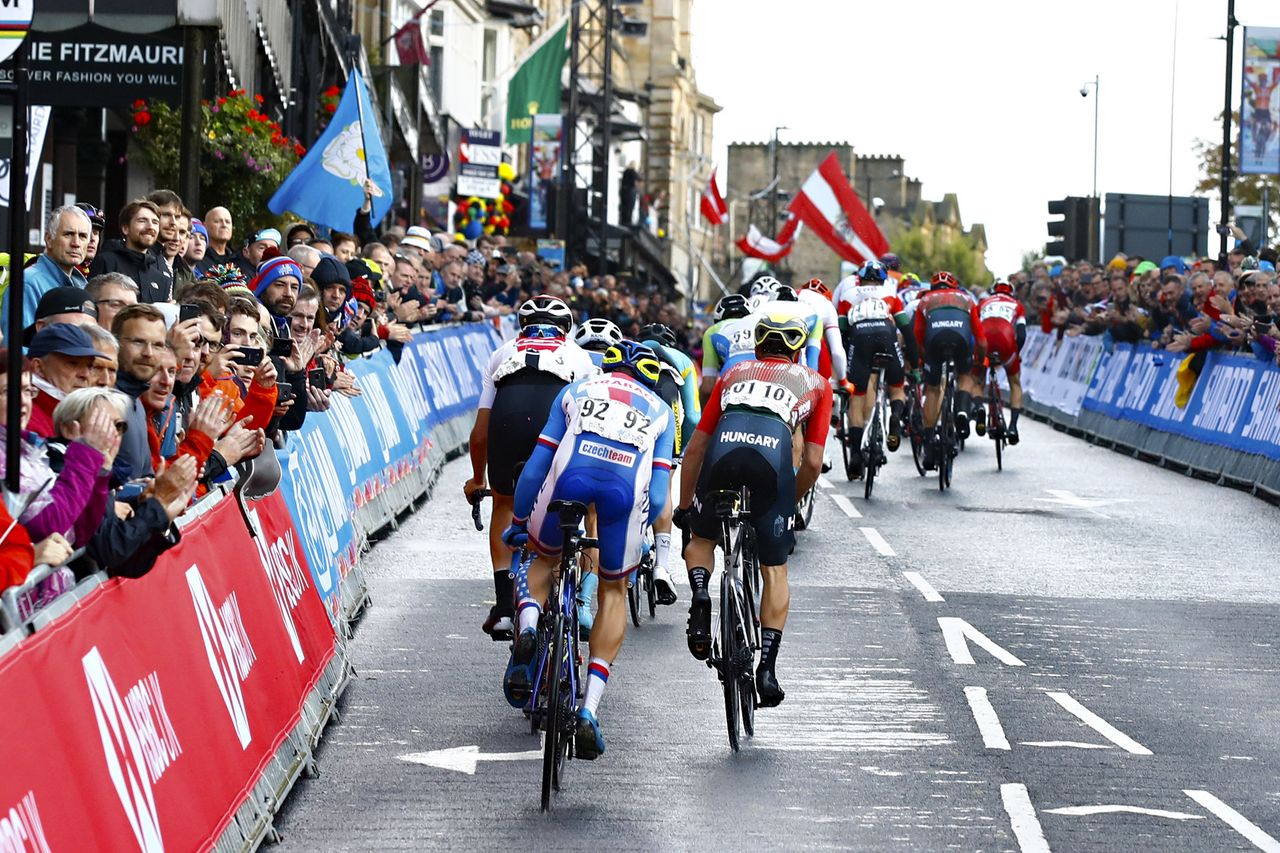 The U23 peloton is strung out passing through the start/finish