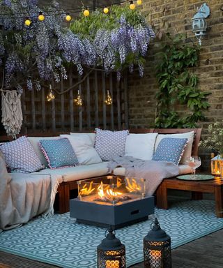A deck idea with purple wysteria tree, fire pit and purple and blue assorted cushions with outdoor rug