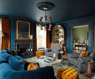 dark living area with deep blue walls and plsuh blue velvet sofa and patterned armchairs