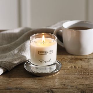 the White Company home scents Fireside candle on a wooden table next to a mug of coffee