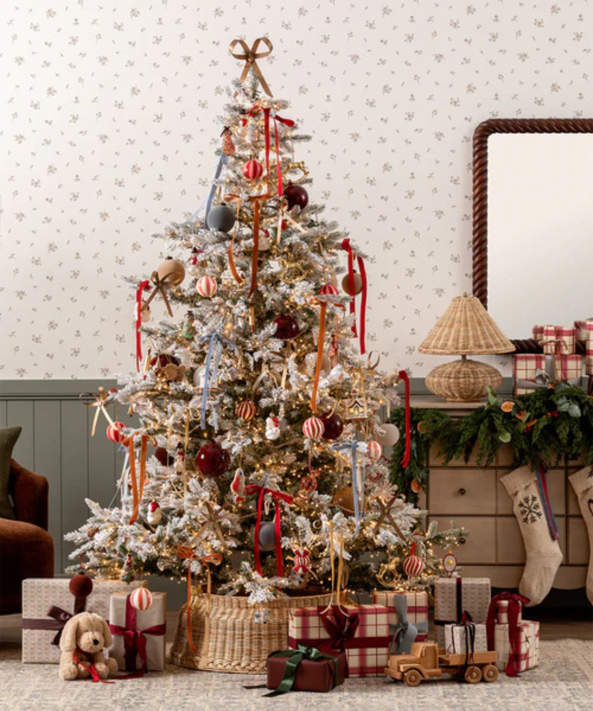 Whimsical christmas tree decorated with bows and glass ornaments surrounded by presents and a console table with rattan light and stocking