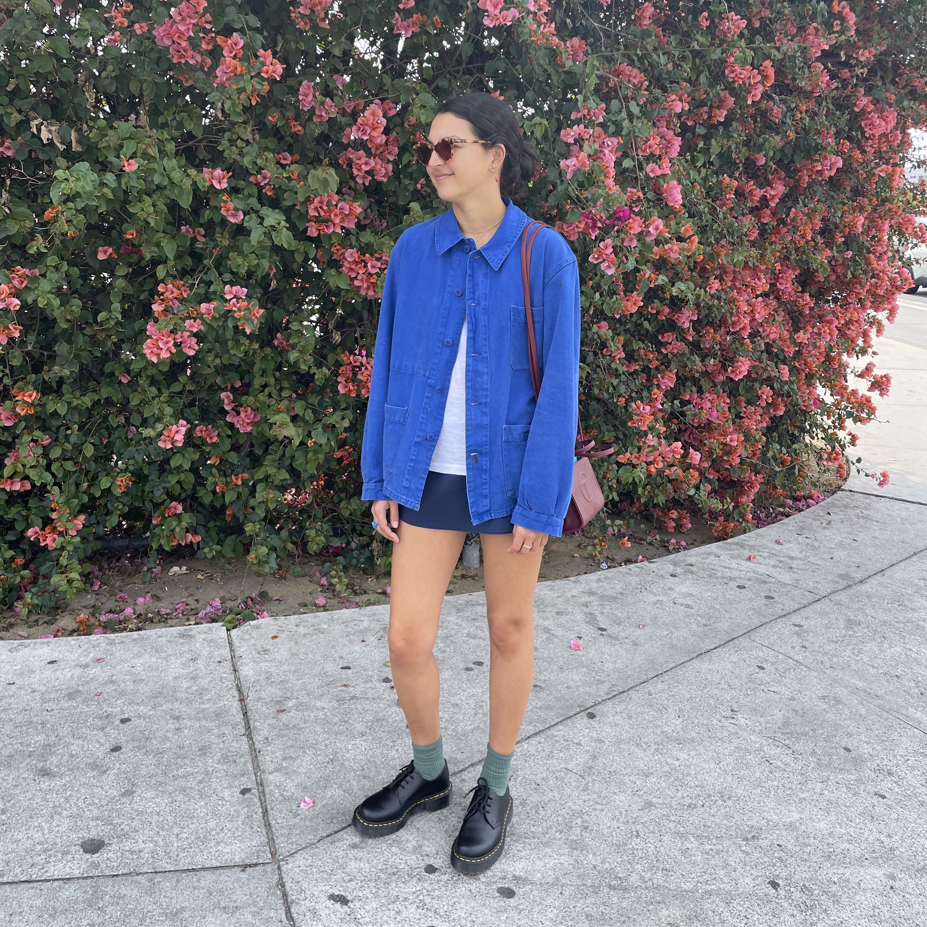 Woman in a blue chore jacket, a black skort, and Dr. Martens loafers.
