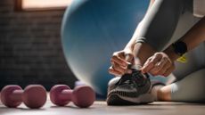 best dumbbells: woman tying shoe lace with dumbbells next to her feet