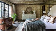 A large countryside bedroom with an exposed brick wall, a wall of windows, and a freestanding copper bath
