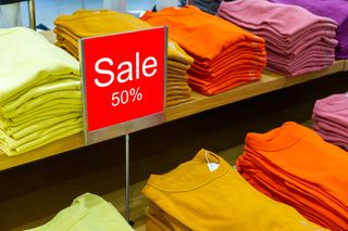 Sale sign with piles of folded sweaters in a shop