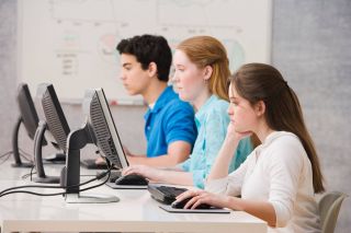 Three teens work at desktop computers in the classroom.
