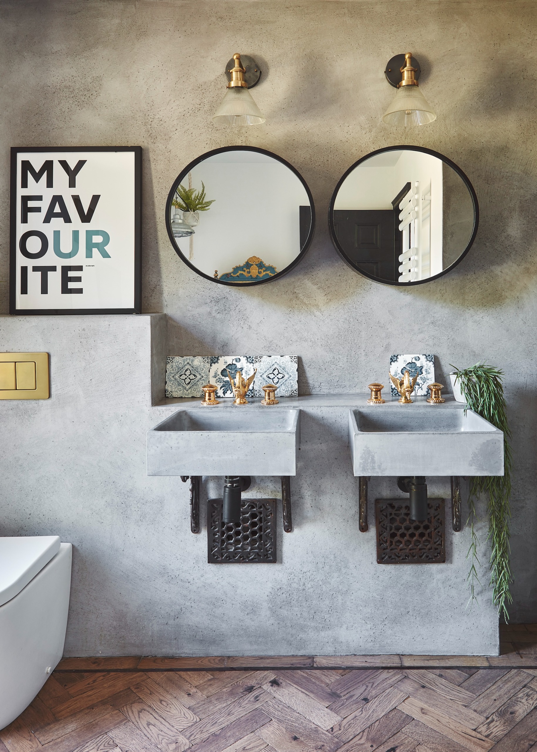 a modern industrial style bathroom with a pair of concrete wall-hung basins and herringbone flooring